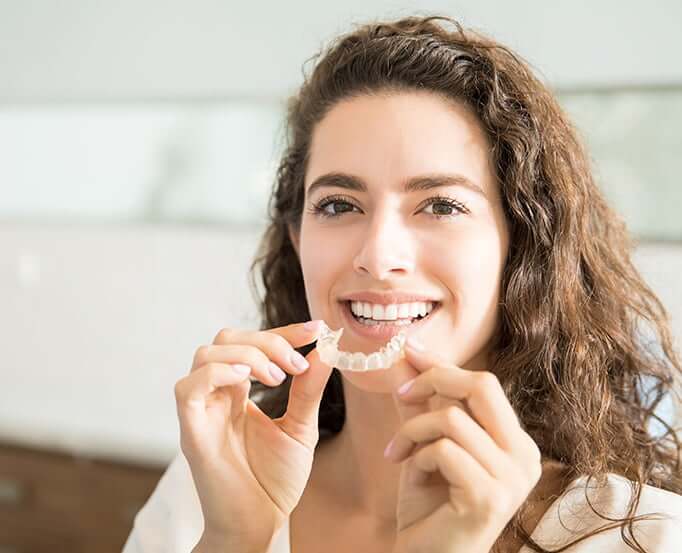 woman inserting clear aligners onto her teeth