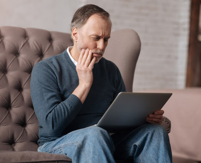 man holding his  jaw in pain while looking at his laptop